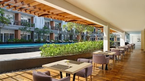 A restaurant with outdoor seating overlooking a swimming pool and a multi-story building with balconies. - Fairfield by Marriott Bali Kuta Sunset Road (Kuta)