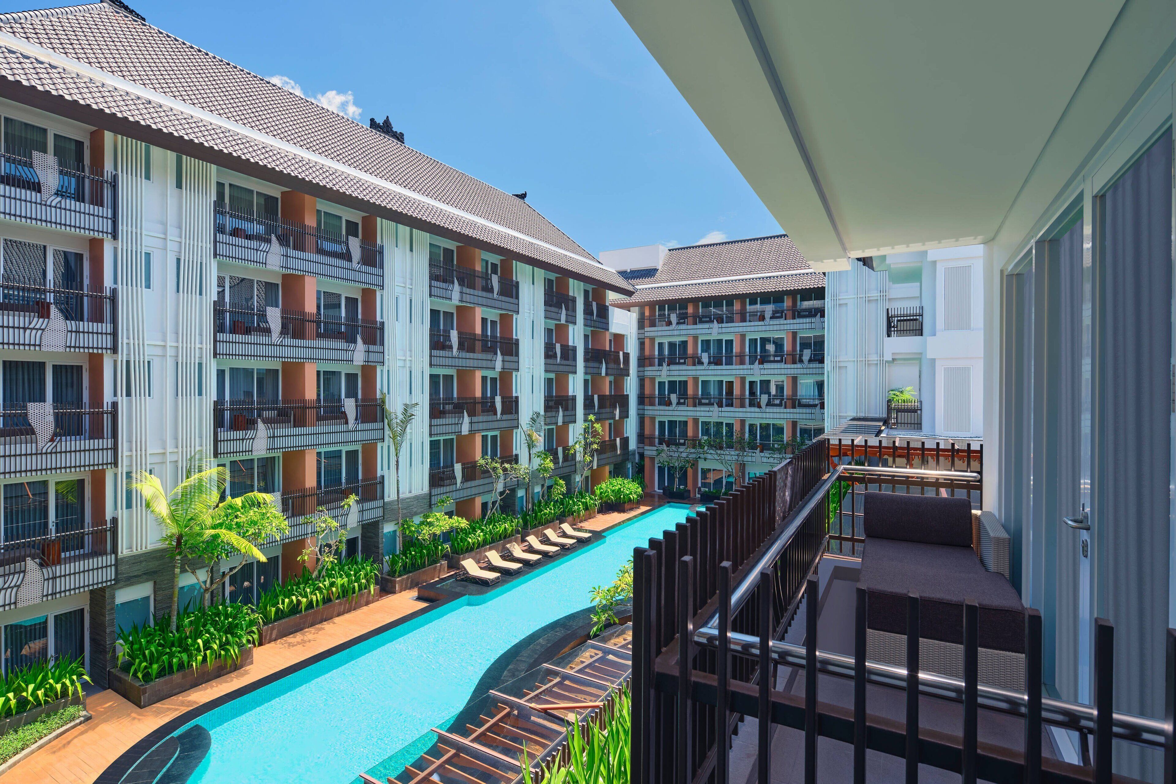 A hotel with multiple balconies, a swimming pool, and lush greenery.