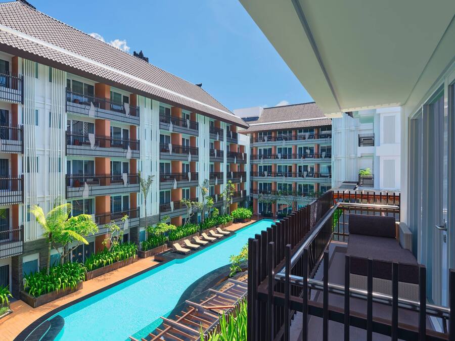A hotel with multiple balconies, a swimming pool, and lush greenery.