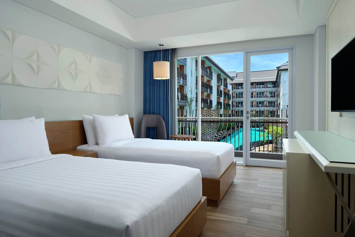 Une chambre d’hôtel avec deux lits, une télévision, un bureau et un balcon donnant sur la piscine.