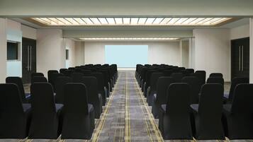A conference room with rows of black chairs, a patterned carpet, and a skylight ceiling.