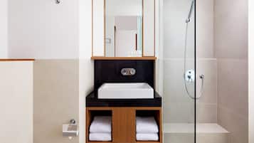 Un baño moderno con un lavamanos blanco, encimera negra, armario de madera y una mampara de cristal.