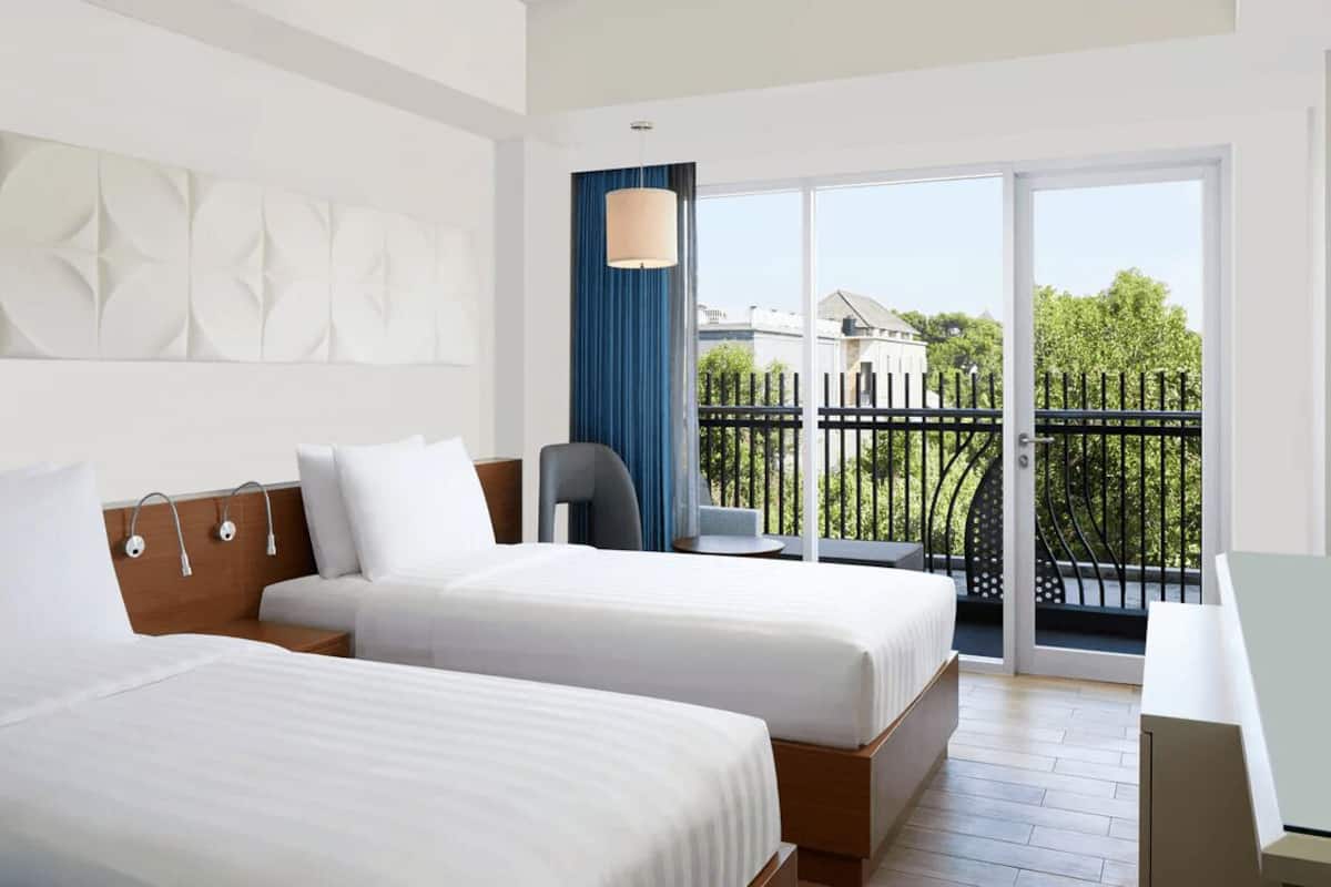 Une chambre d’hôtel avec deux lits, une télévision, un bureau et un balcon donnant sur une clôture et des arbres.