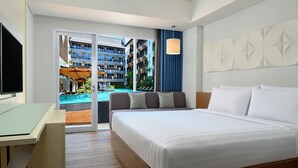 A hotel room with a bed, a desk, a TV, and a view of a pool and building. - Fairfield by Marriott Bali Kuta Sunset Road (Kuta)