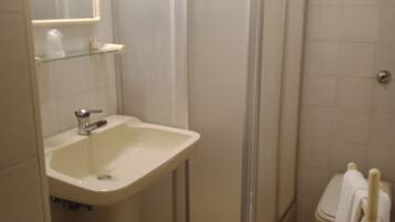 Un baño con lavamanos, espejo, cabina de ducha, inodoro y toallero.