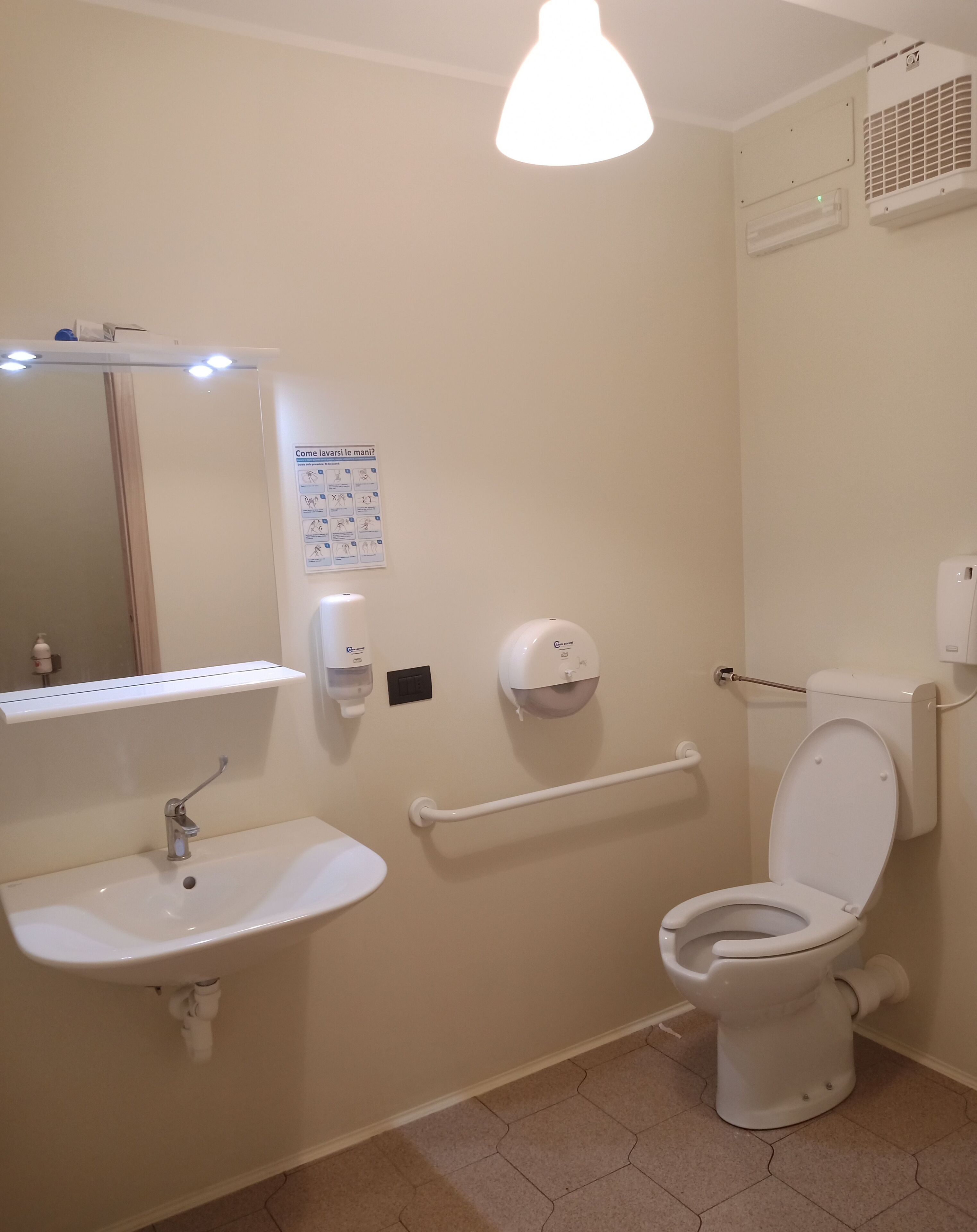 Ein Badezimmer mit Waschbecken, Spiegel, Toilette, Händetrockner und Handdesinfektionsmittelspender.
