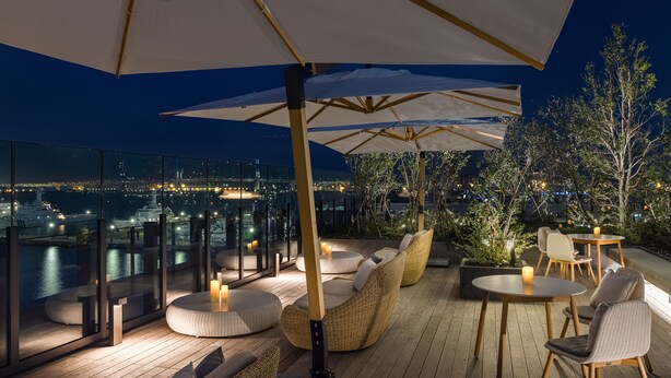 Una terraza en la azotea con mobiliario exterior, sombrillas y vistas nocturnas de la ciudad.