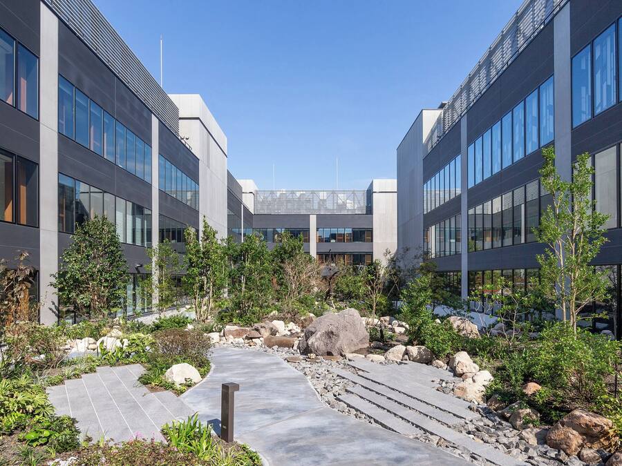 A modern building with large windows and a central courtyard with a pathway, surrounded by greenery and rocks.