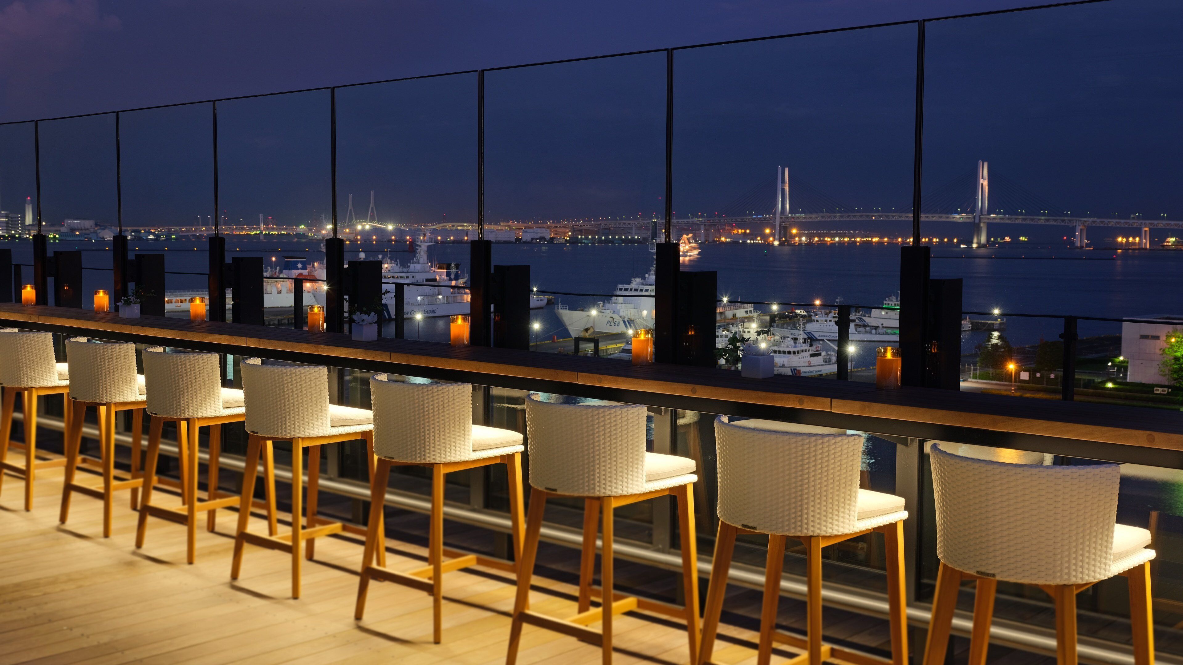 A bar area with wicker chairs and a view of a bridge at night.