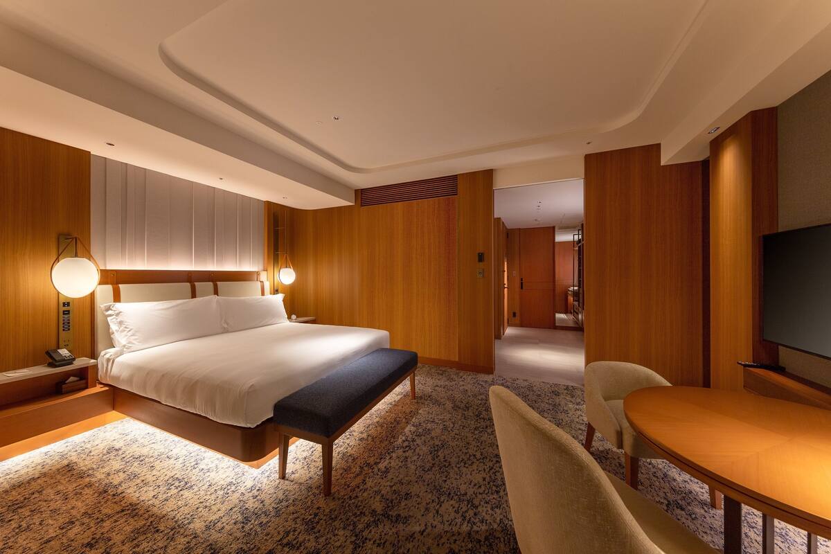 A hotel room with a large bed, bedside lamps, a desk with a chair, and a television.