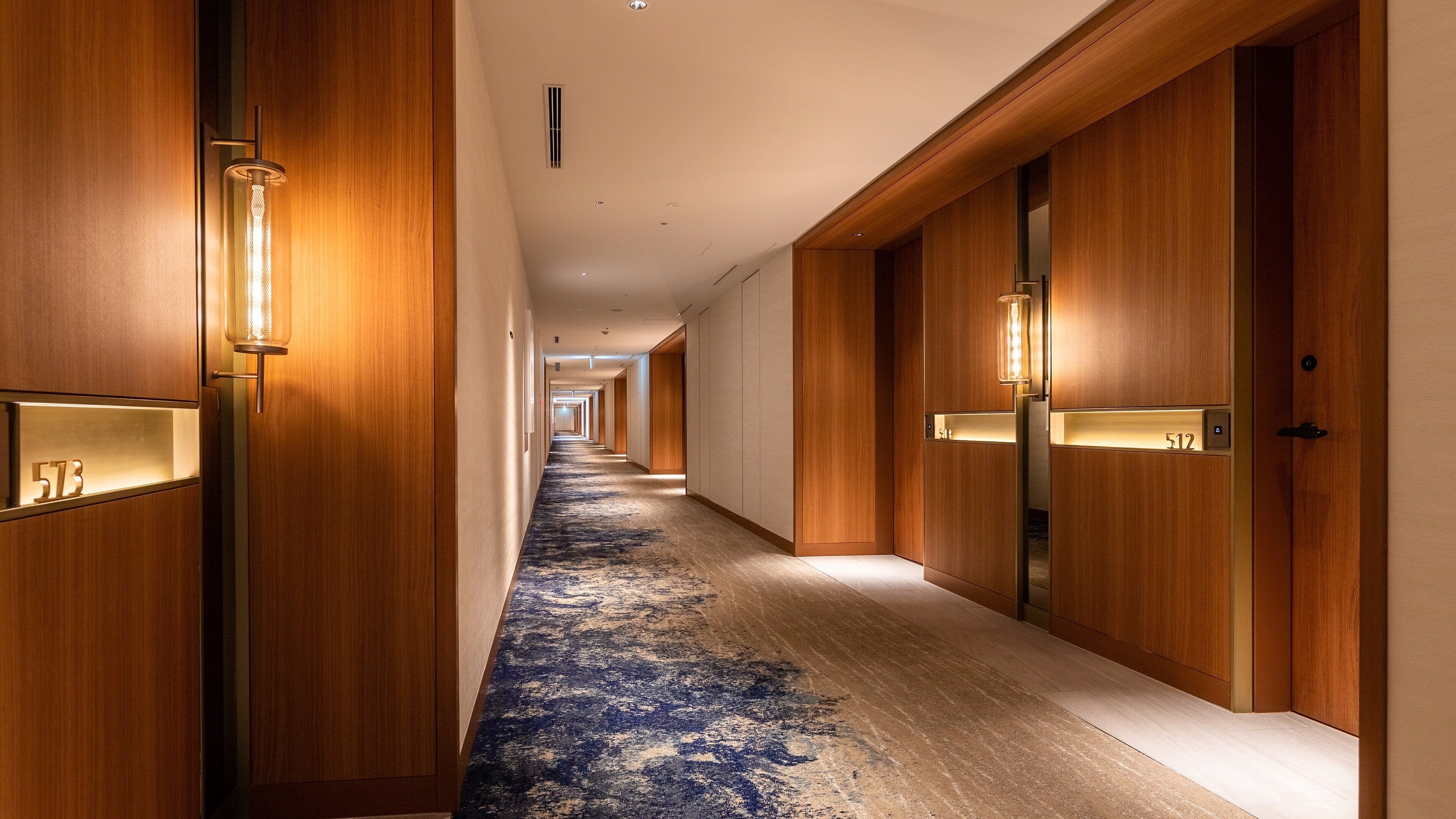 A hotel hallway with wooden doors, illuminated number plates, and a patterned carpet.