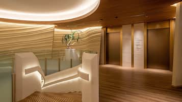 A modern interior with a reception desk, a glass partition, a potted plant, and a wall-mounted elevator control panel.