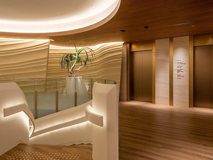 A modern interior with a reception desk, a glass partition, a potted plant, and a wall-mounted elevator control panel.