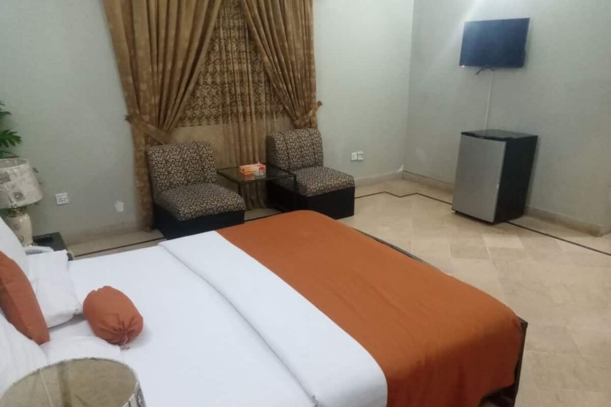 Ein Hotelzimmer mit einem Bett, zwei gemusterten Sesseln, einem kleinen Tisch, einem Fernseher und einem Schrank.