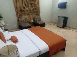 Habitación de hotel con cama, dos sillones estampados, una mesita, televisor y armario.