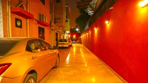 A narrow alleyway with parked cars and a red wall on one side. - Luxury Inn (Karachi)