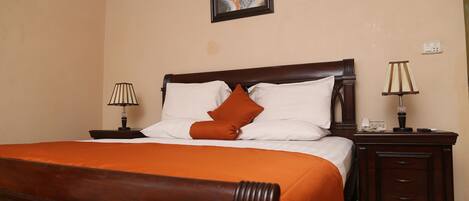 A neatly made bed with an orange bedspread and two pillows, a wooden nightstand with a lamp, and a wall-mounted picture.