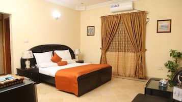 A hotel room with a bed, nightstands, a lamp, a plant, and a window with curtains.