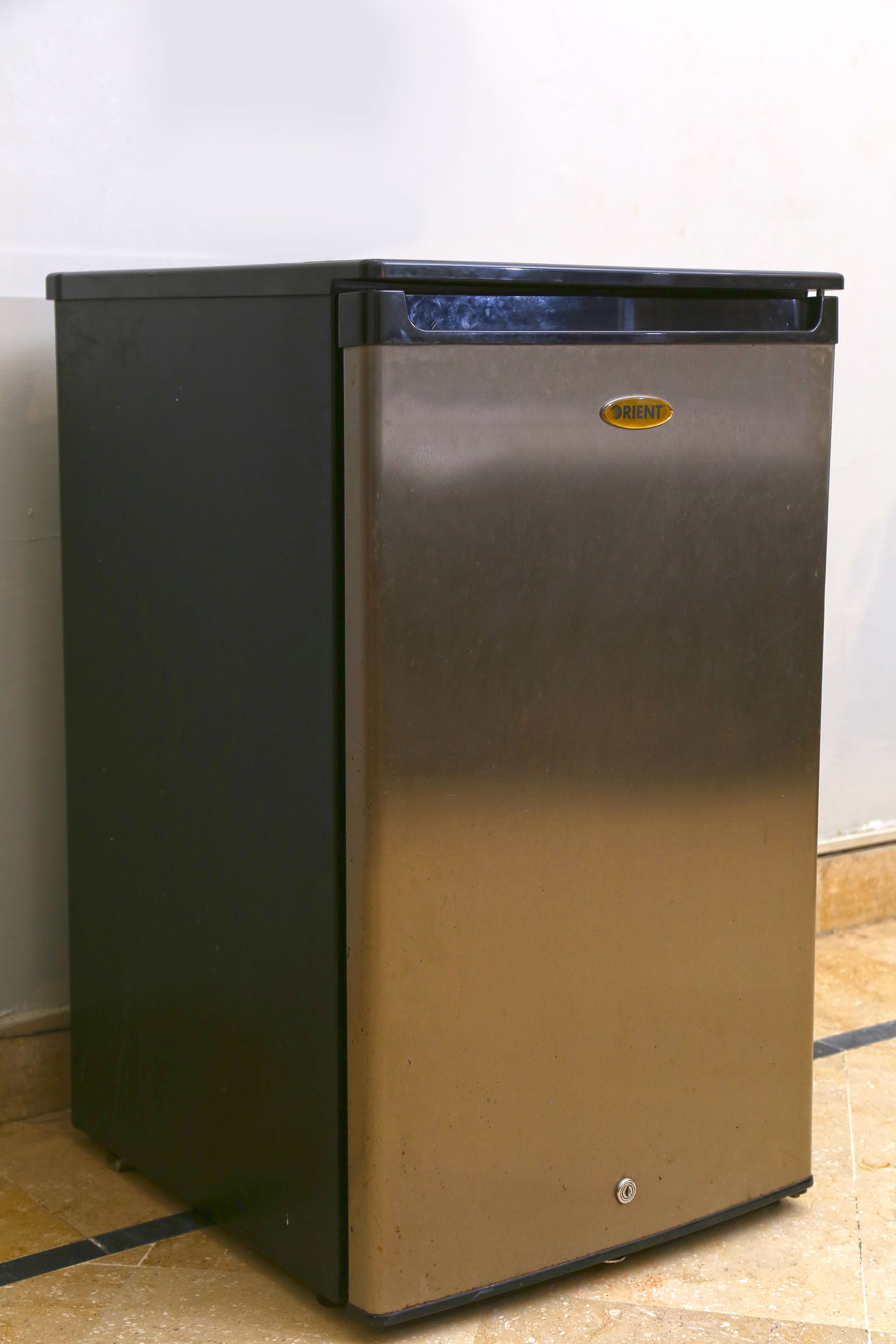 Un refrigerador metálico compacto con parte superior negra y base de acero inoxidable, que muestra el logo de la marca.