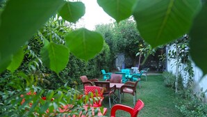 A garden patio with tables and chairs, surrounded by greenery and a stone wall. - Luxury Inn (Karachi)