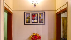 A hallway with a glass table and a vase of flowers, framed artwork on the wall, and wooden trim. - Luxury Inn (Karachi)