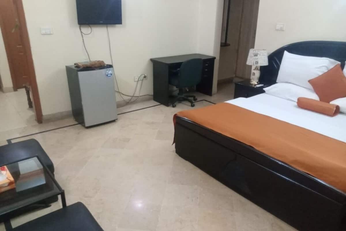 Ein Hotelzimmer mit Bett, Schreibtisch, Stuhl, kleinem Kühlschrank und Wandfernseher.