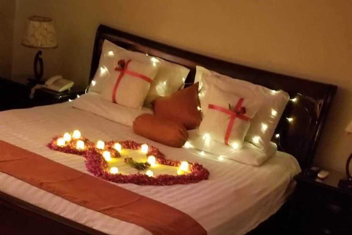 Ein ordentlich bezogenes Bett mit einer herzförmigen Anordnung aus Kerzen und Rosenblättern auf dem Boden.