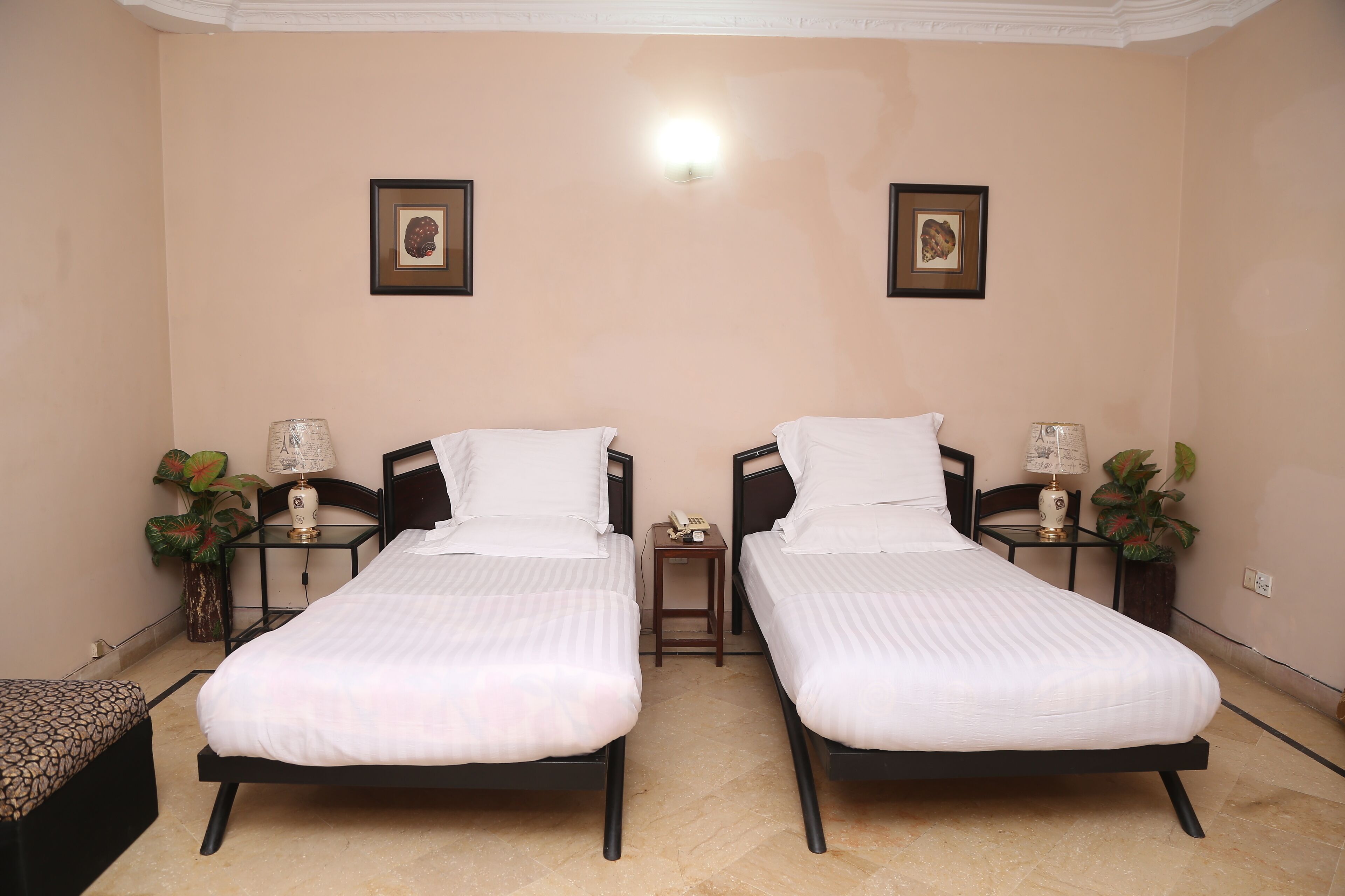 A room with two single beds, a small table with a lamp, and two wall-mounted lamps.