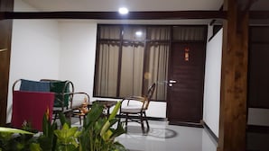 A room with a dining table and chairs, a window with curtains, and a door with a sign. - Trawangan Cottages (Gili Trawangan)