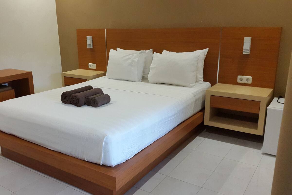 A modern hotel room with a large bed, two bedside tables, and a small wooden nightstand.