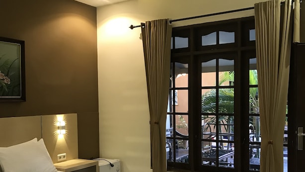 A hotel room with a large bed, a bedside table, a wall-mounted light, and a window with curtains. - Trawangan Cottages (Gili Trawangan)
