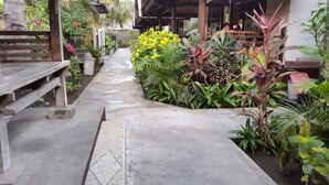 A concrete pathway leading to a covered area with wooden benches and potted plants. - Trawangan Cottages (Gili Trawangan)