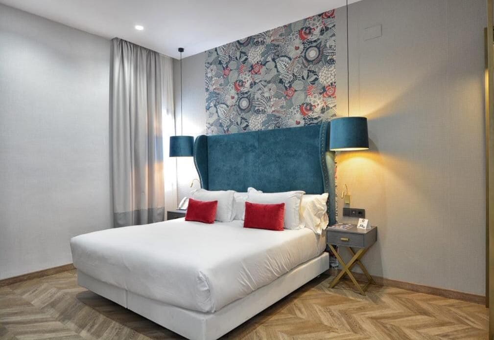 Une chambre d’hôtel moderne avec un grand lit, une table de chevet, une lampe et un mur décoré d’un motif.