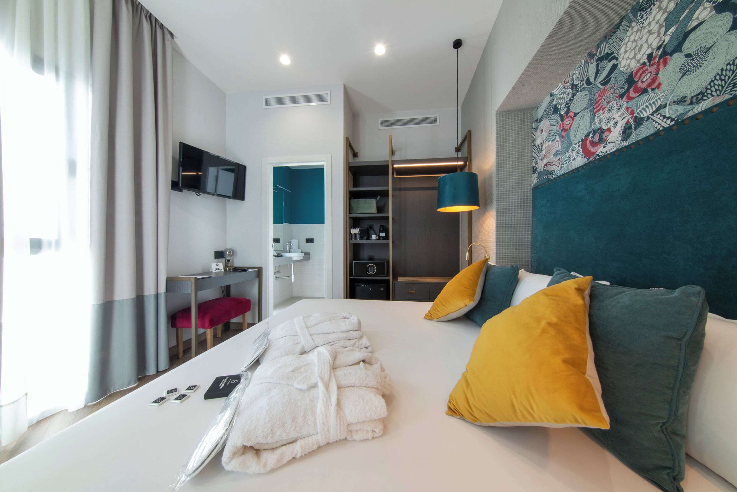 Habitación de hotel moderna con una cama bien hecha, un escritorio con silla, un armario y un televisor montado en la pared.