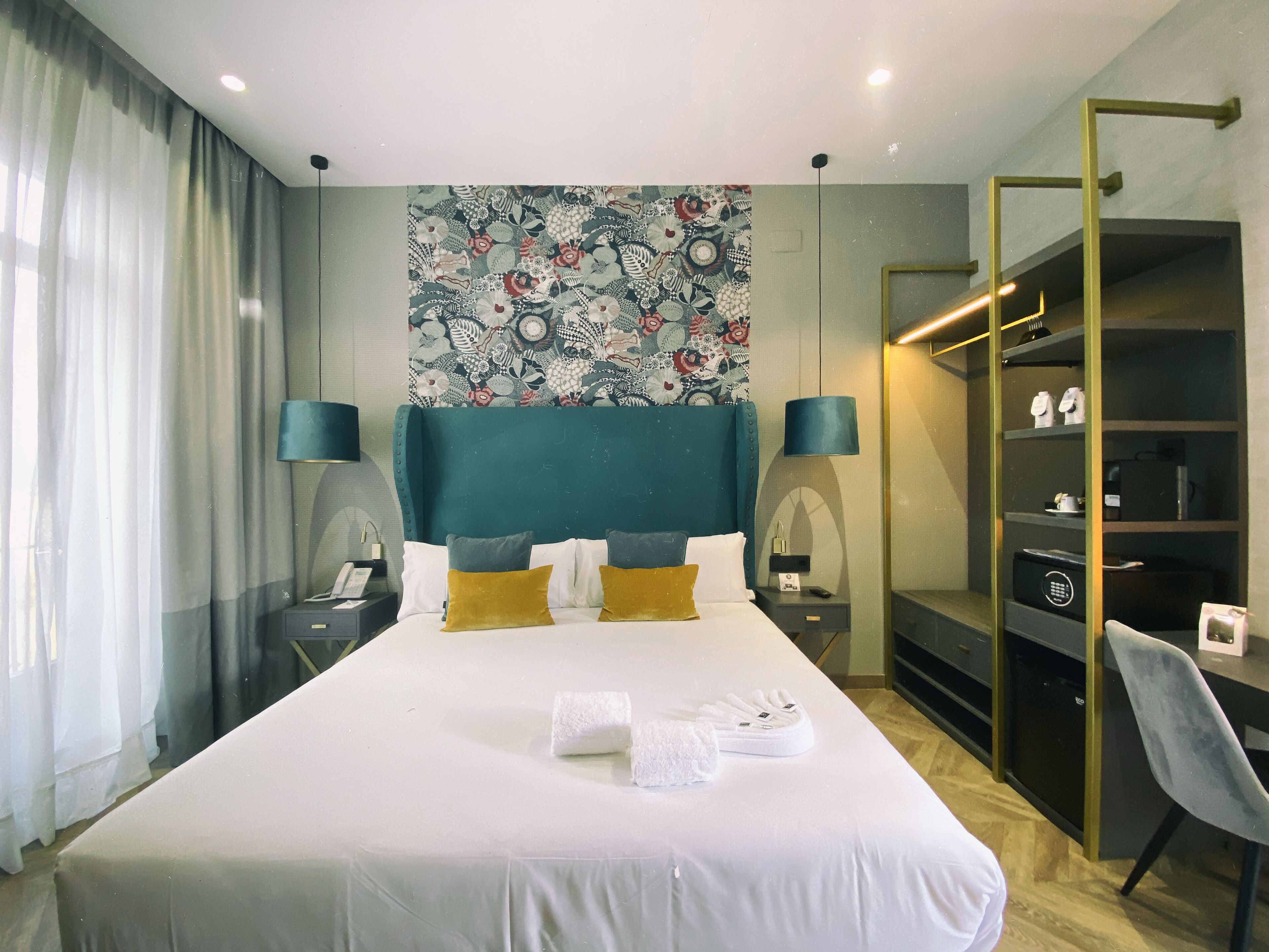 Une chambre d’hôtel avec un grand lit, deux tables de chevet, un bureau, une chaise, une armoire et une tapisserie murale décorative.