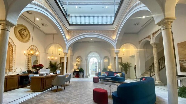 A spacious lobby with a high ceiling, a central seating area with sofas, a reception desk, and a staircase leading to an upper level. - Soho Boutique Sevilla (Seville)