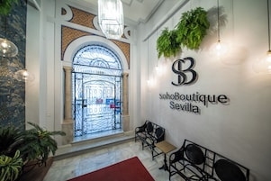 Entrada de un hotel boutique con una reja de hierro forjado, zona de estar y un letrero en la pared que dice 'sohoBoutique Sevilla'.