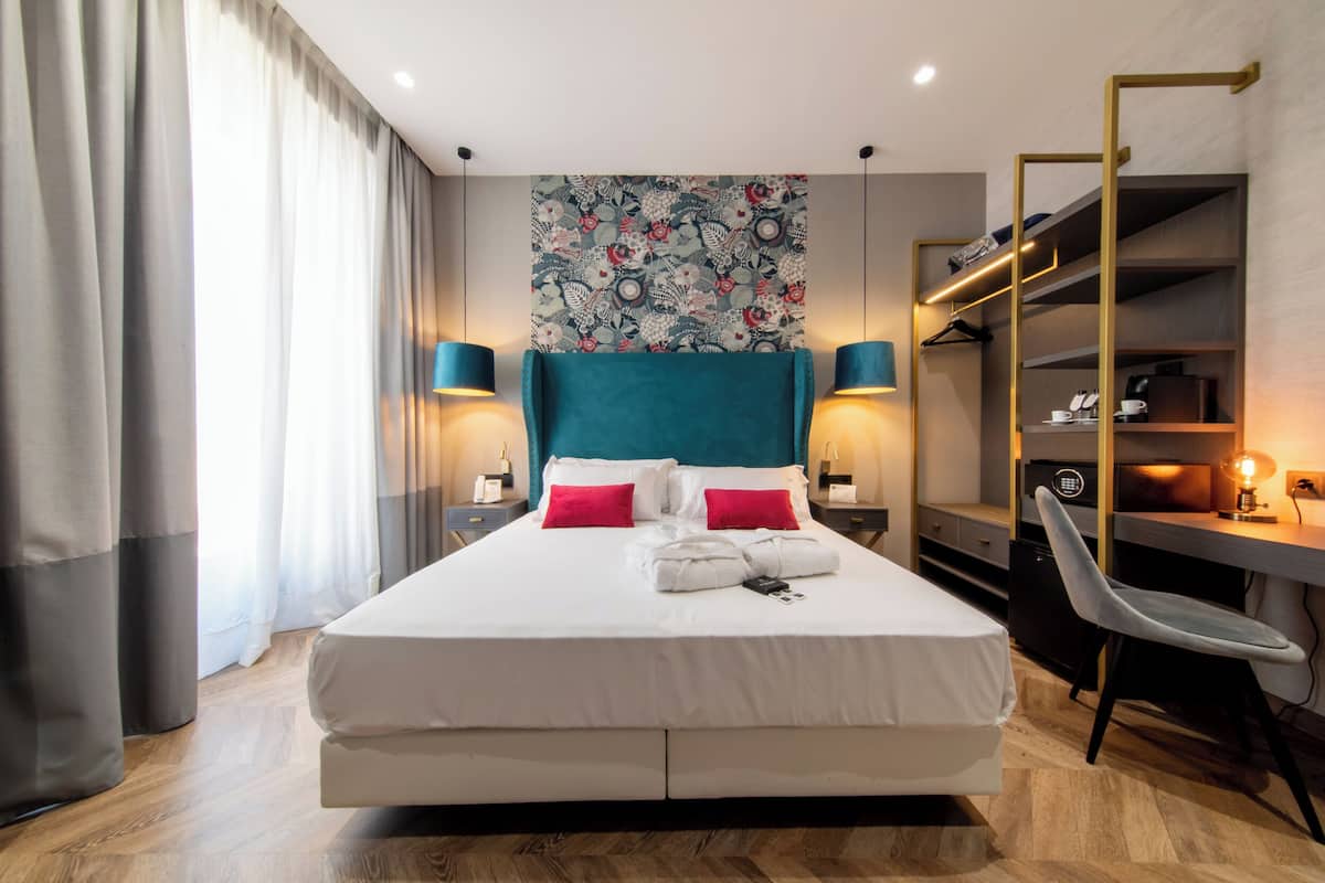 A modern hotel room with a large bed, a desk, and a wardrobe.