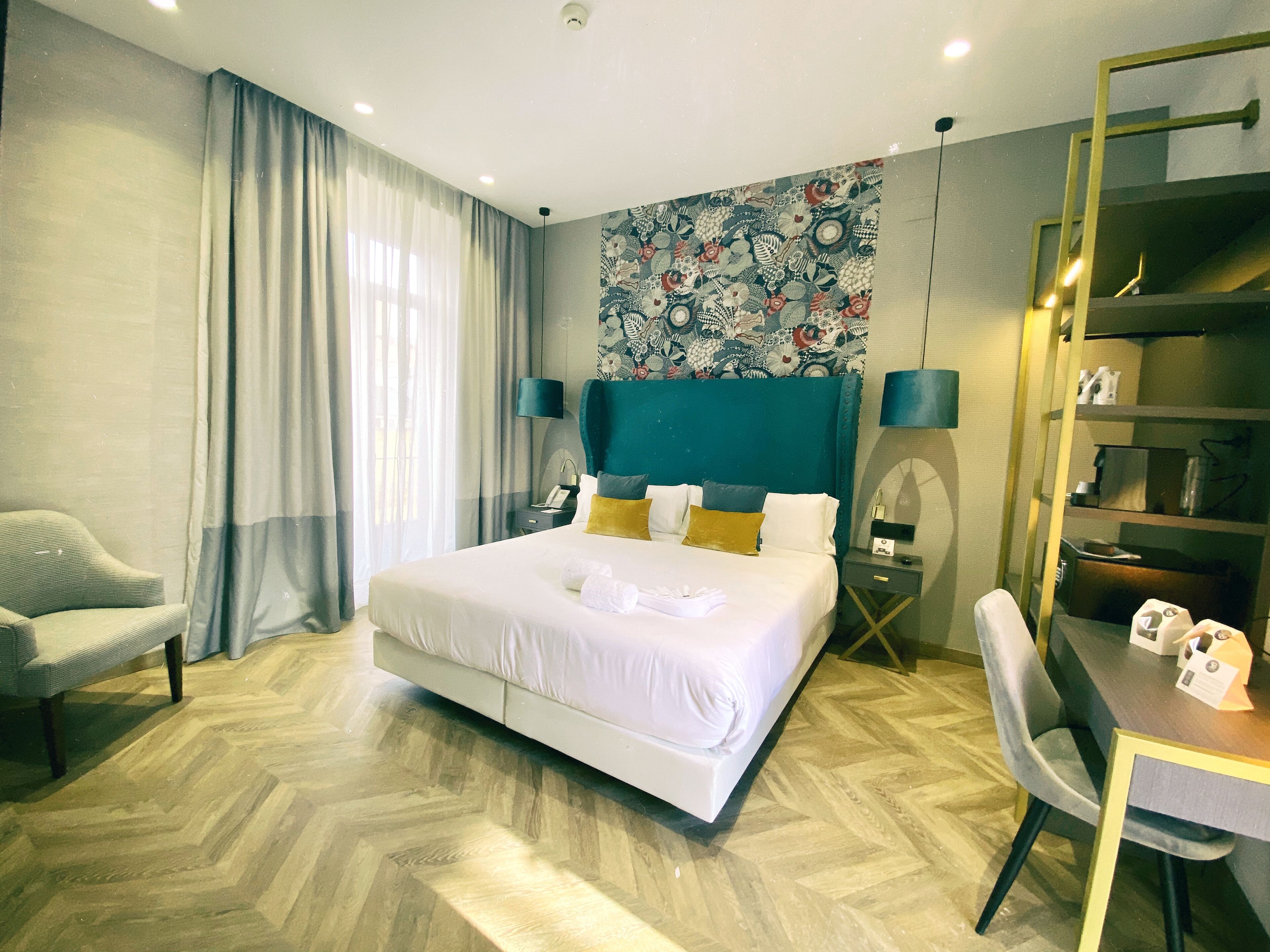 Una habitación de hotel con una cama grande, un escritorio con una silla, una mesita pequeña y una estantería.