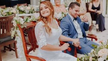 A wedding ceremony with a bride and groom seated on wooden chairs adorned with floral arrangements.