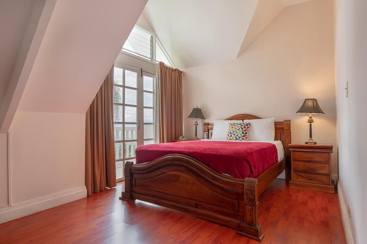 A bedroom with a wooden bed, a nightstand, a lamp, and a window with curtains.