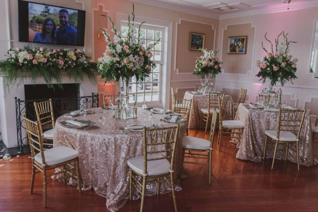 A formal dining room with round tables, gold chairs, and floral centerpieces.