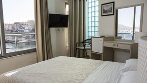 A hotel room with a bed, a desk, a chair, a TV, and a window with a city view. - Hotel Titania (Sarandë)