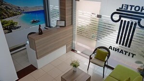 A hotel reception area with a wooden reception desk, a chair, a small table with a plant, and a wall with a large 'HOTEL' sign. - Hotel Titania (Sarandë)