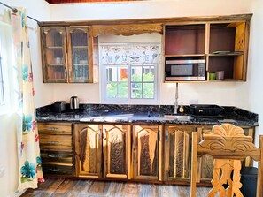 A kitchen with wooden cabinets, a black countertop, a window with a view, and a microwave. - Yoga Dreams Negril (Negril)