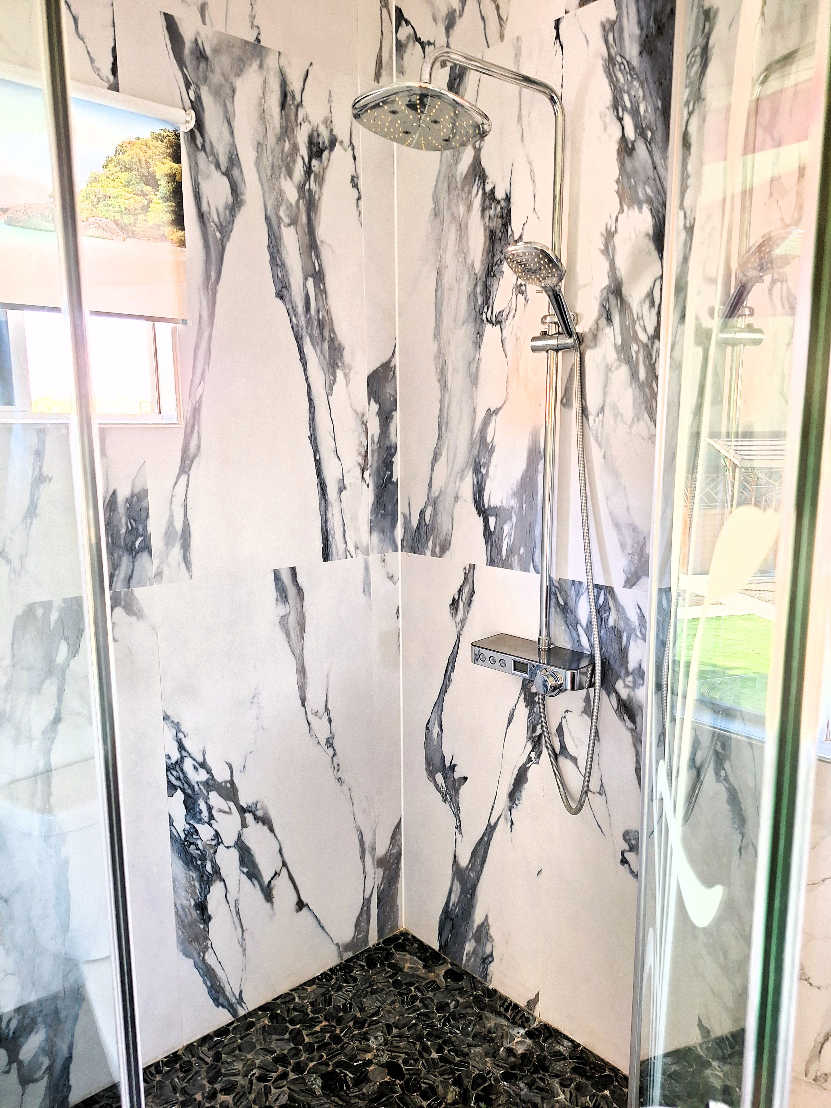 Una ducha con puerta de vidrio, paredes de mármol y piso negro.