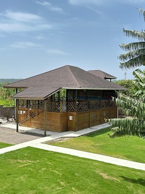 A wooden building with a sloped roof, a covered outdoor area with a staircase, and a grassy lawn. - Yoga Dreams Negril (Negril)