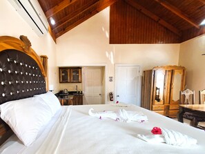 A hotel room with a large bed, a wooden headboard, a wooden wardrobe, a small table, and a kitchenette in the background. - Yoga Dreams Negril (Negril)