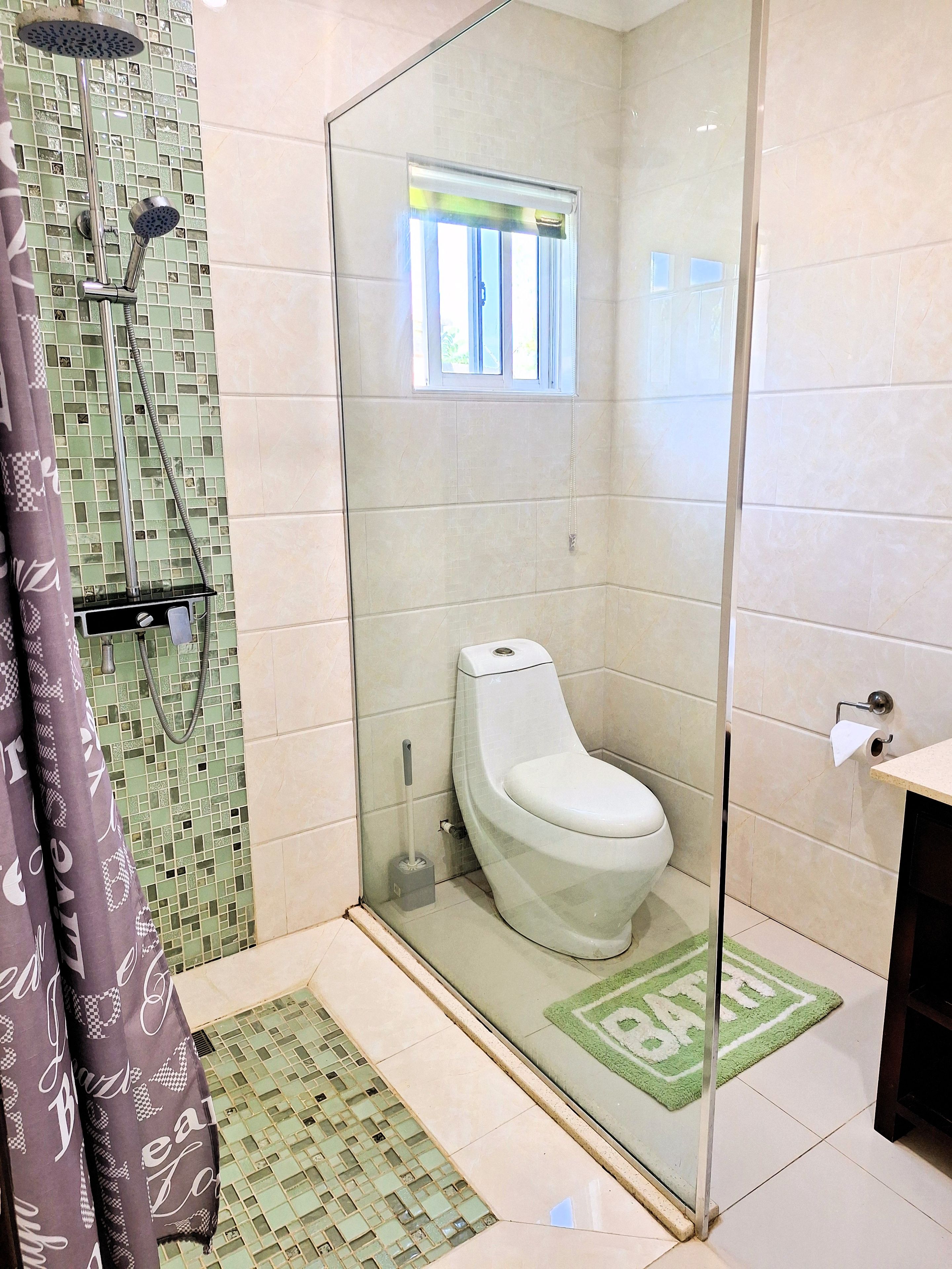 Une salle de bain avec une douche à parois de verre, des toilettes et une petite fenêtre.