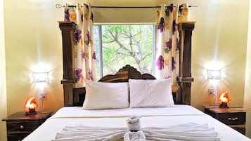 A hotel room with a bed, floral curtains, bedside lamps, and a view of greenery outside.